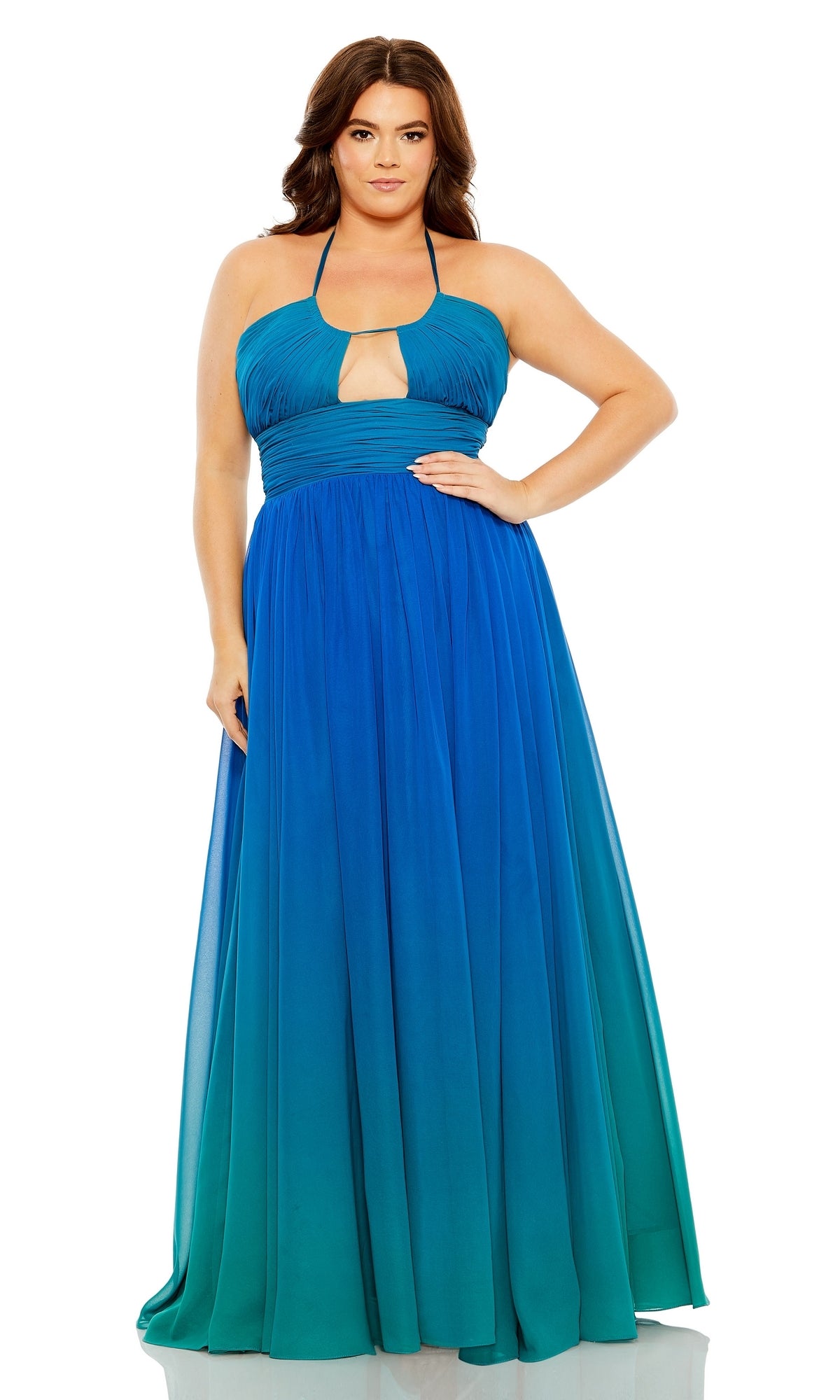 A woman stands with one hand on her hip wearing the Long Plus-Size Formal Dress 77017 by Mac Duggal, featuring a sleeveless halter neck, blue-green ombre design, and keyhole cutout against a white background.